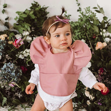 Load image into Gallery viewer, Snuggle Hunny Kids - Primrose Frill waterproof bib worn by a baby with a headband on and flowers behind her