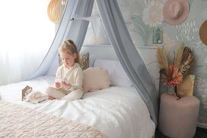 girl sitting on double bed with grey canopy above bed
