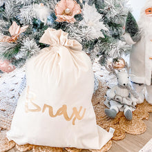 Load image into Gallery viewer, Ivory personalised santa sack with the name Brax written in metallic gold font. The sack is sitting under the christmas tree with peach and white decorations.