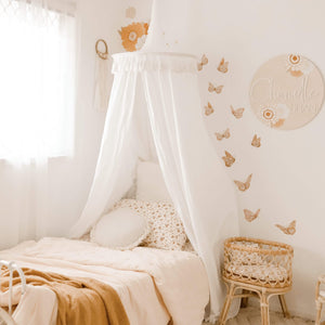 White round canopy over bed in girls boho room with butterfly decals and rattan doll bassinet