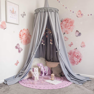 Grey round canopy over reading nook area with rose decals on wall and pink crochet rug on floor with purple toy horse