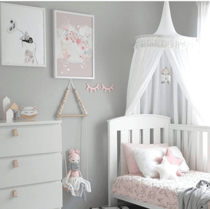 White round canopy hanging over timber white cot in nursery with grey walls and framed prints and timber toys