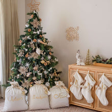Load image into Gallery viewer, ivory santa sacks and christmas stockings sitting next to a christmas tree decorated with gold decorations and flowers.