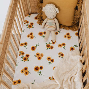 Snuggle Hunny Kids Sunflower Fitted Cot Sheet shown on a cot bed with throw , soft lamb toy and tassel cushion on top