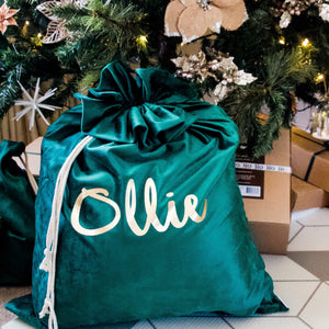 green santa sack personalised with the name ollie in gold font sitting under a christmas tree