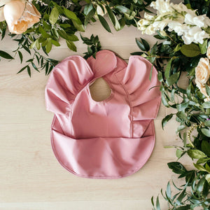 Snuggle Hunny Kids - Primrose Frill waterproof bib shown with flowers around it on a table 