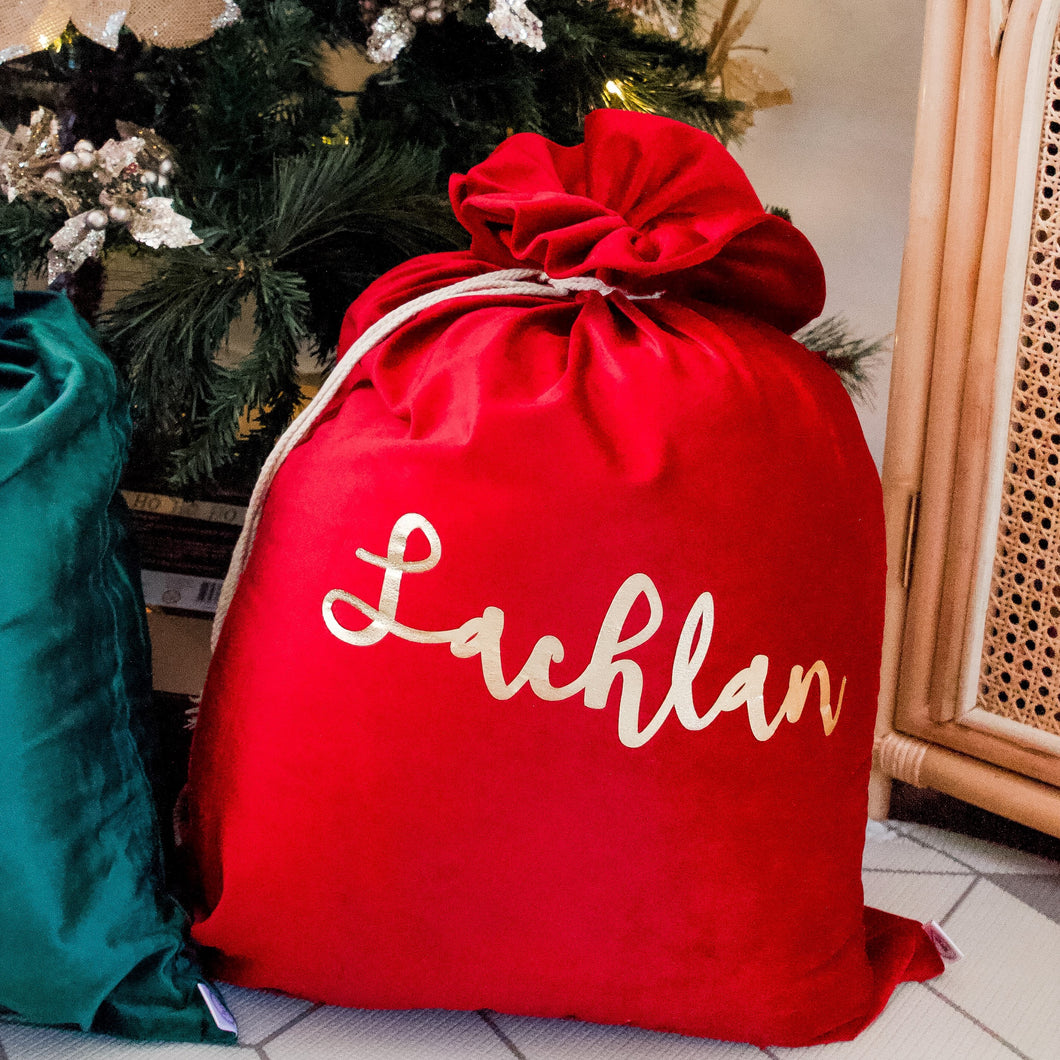 red santa sack personalised with the name lachlan sitting next to a green sack under a christmas tree