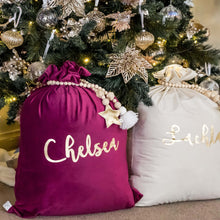 Load image into Gallery viewer, purple and ivory santa sacks sitting under a green christmas tree. The sacks are personalised with a beaded garland wrapped around the top. The tree is decorated with gold decorations 