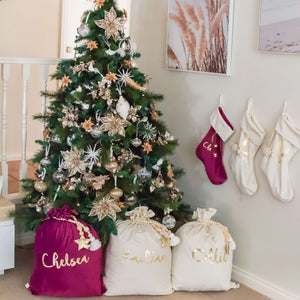 Magenta and ivory santa sacks sitting under a christmas three with three stocking hanging on the wall