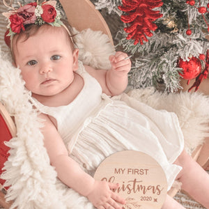 baby girl holding a mdf round disc engraved with the words my first christmas 