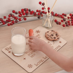 childs hand placing orange carrot onto wooden santa tray with half glass of milk and choc chip cookie