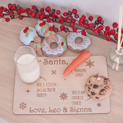 Wooden santa tray sitting on table with half glass of milk, one orange carrot and a choc chip cookie sitting on top