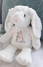 Load image into Gallery viewer, White soft bunny rabbit sitting on bed with long white floppy ears. The name Asher and the Initial A is printed on the bunnys chest with a variety of colourful florals. 