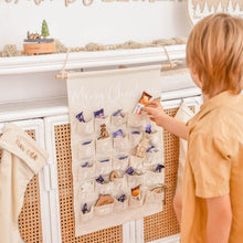 Load image into Gallery viewer, A boy selecting a chocolate treat out of a fabric advent calendar hanging on a shelf