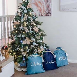 blue and navy santa sacks sitting under a christmas tree personalised in silver metallic font. The tree is decorated with blue and gold decorations.