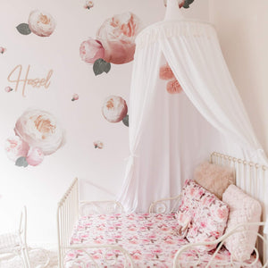 Girls room with white round canopy hanging over wrought iron bed with rose decals on wall and rose bedspread