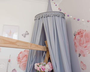 Grey canopy hanging over timber house bed with pink wall decals and floral mobile