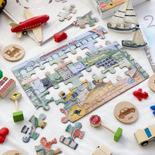 Load image into Gallery viewer, half complete puzzle laying on table with wooden cars, planes, boats and toys around the puzzle