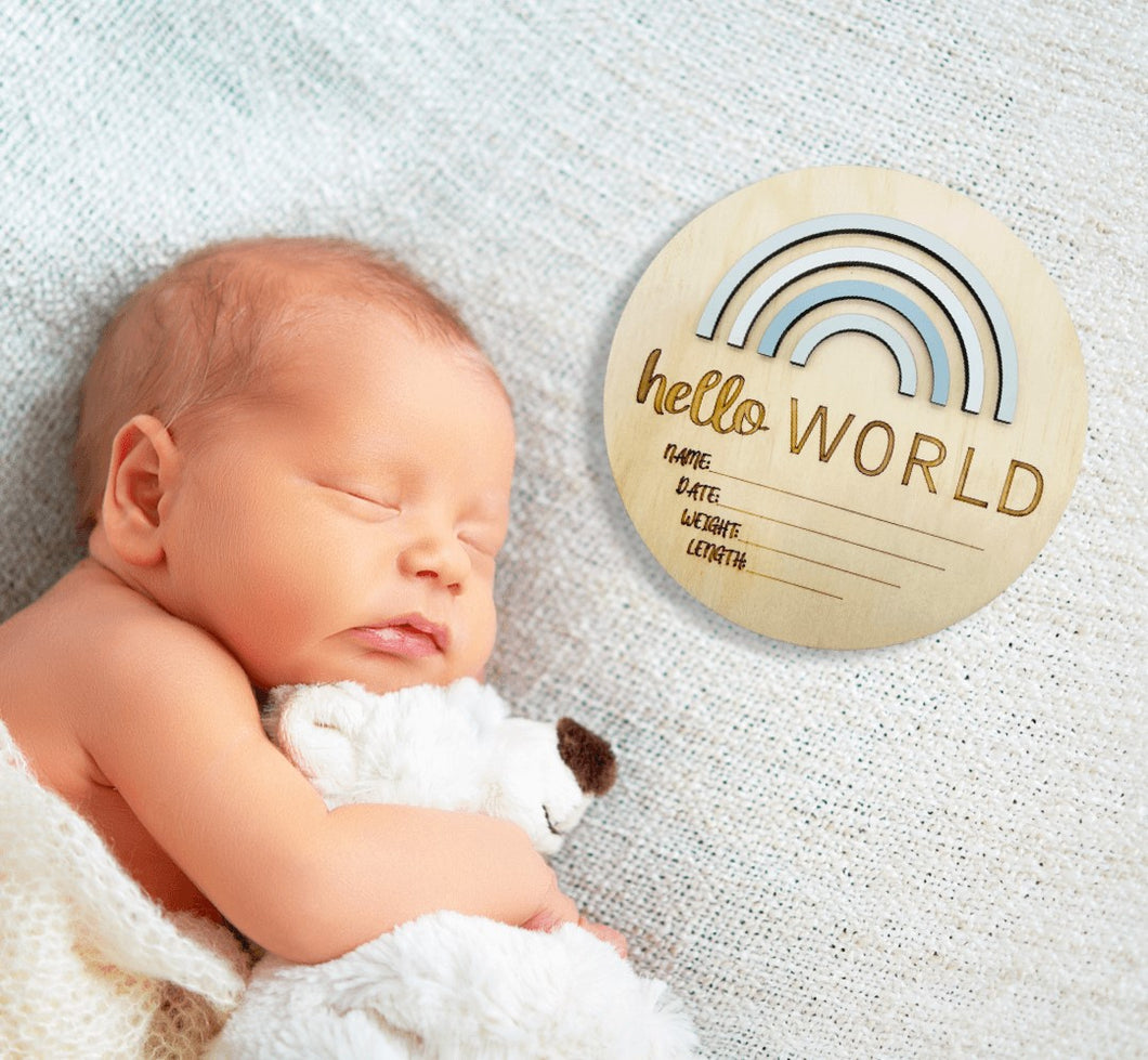 baby asleep on blanket hugging soft toy with round wooden birth announcement plaque laying next to him