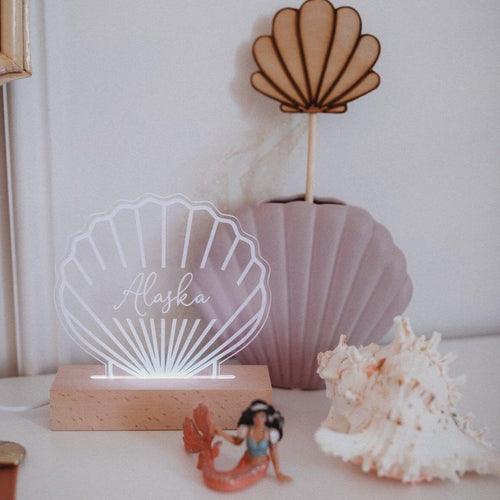 shell shaped personalised night light with the name Alaska engraved onto it shitting next to a shell and a vase