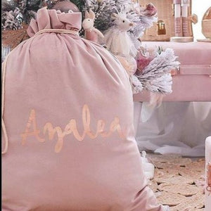 Blush pink santa sacks personalised with the name Azalea in rose gold font sitting in a girls bedroom