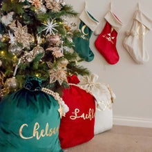 Load image into Gallery viewer, red, green and white personalised santa sacks sitting under a green christmas tree. A red, green and white stocking is on the wall next to the tree. 