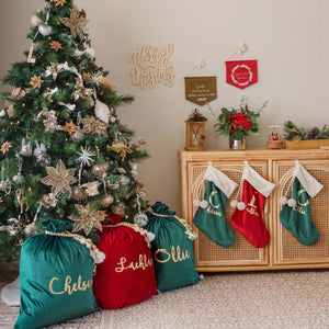 three christmas santa sacks sitting under a green decorated christmas tree