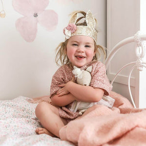 toddler on bed with gold sequin cunny crown on head and holding soft toy