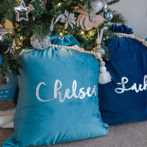 Turquoise and navy blue santa sacks sitting under a christmas tree. 
