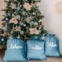 Load image into Gallery viewer, Three turquoise santa sacks sitting under a christmas tree personalised with names in silver writing.