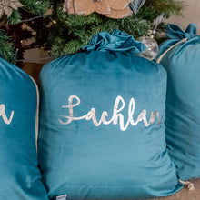 Load image into Gallery viewer, three turquoise blue santa sacks sitting under a christmas tree. The middle sack in personalised with the name Lachlan written in silver metallic font. 
