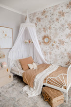 Load image into Gallery viewer, White round canopy over white wrought iron bed with featured wall of rose wallpaper and dusty peach bedspread and pillow and rattan mirror and chest