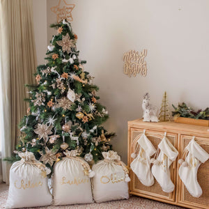 white personalised santa sacks and stockings sitting under a green christmas tree in the corner of a lounge room