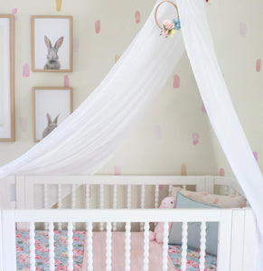 white drape canopy hanging above white cot with bed and pink bedding and pictures of rabbits on the wall
