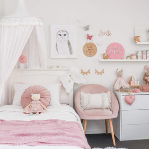 White round canopy sitting over white timber bed with dusty pink velvet cushion on bed and velvet armchair in a girls room with pink doll and toys
